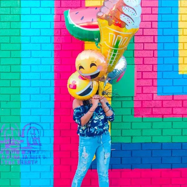A girl celebrates her birthday with balloons in front of a colorful mural.