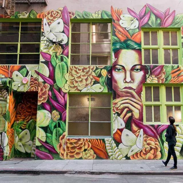 贝博体彩app，一名妇女抬头看着一座华丽建筑侧面色彩鲜艳的壁画.